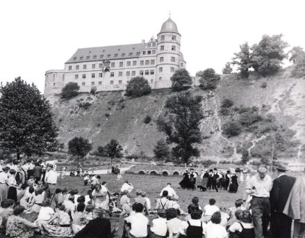 Die zerstörte Wewelsburg 1953 von der Almewiese unterhalb der Burg fotografiert. Viele Paare führen Volkstänze auf und sitzen zuschauend im Gras.